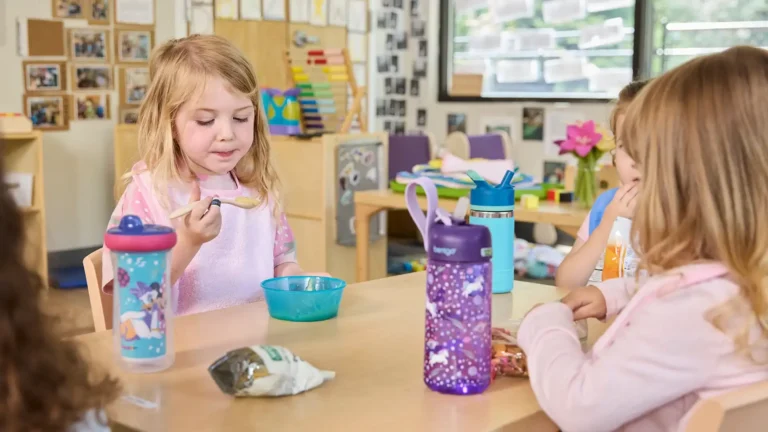 Child holding a spoon wears a pink terrycloth toddler bib while eating with friends