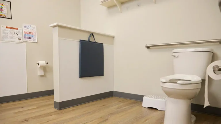 Gray vinyl square changing pad for toddlers hanging in daycare bathroom beside toilet