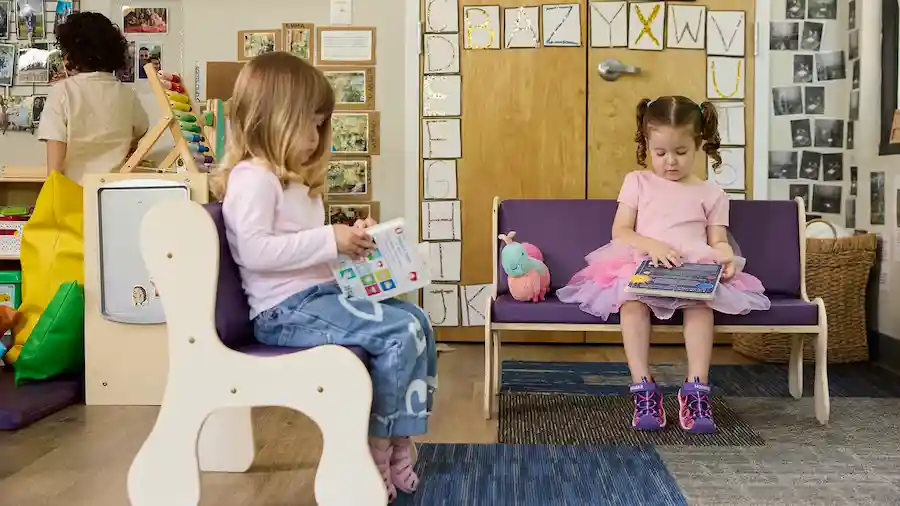 Children sit on a wooden couch and chair with dark purple vinyl cushions in classroom