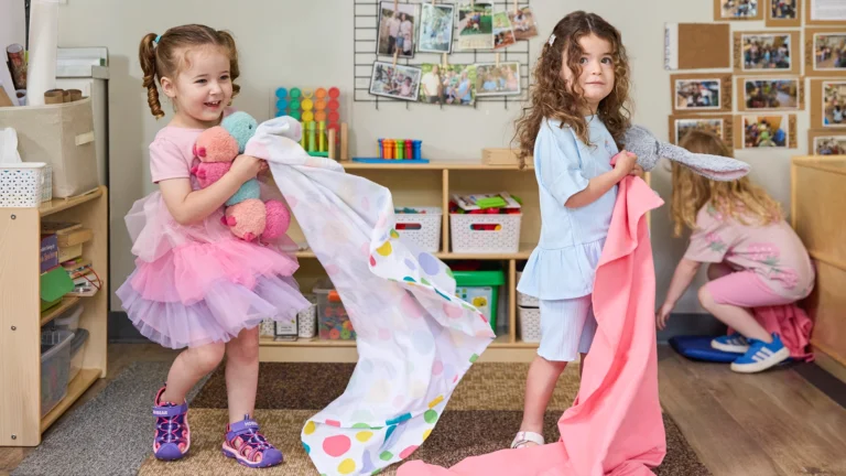 Children holding stuffed toys and flannel blankets in a classroom